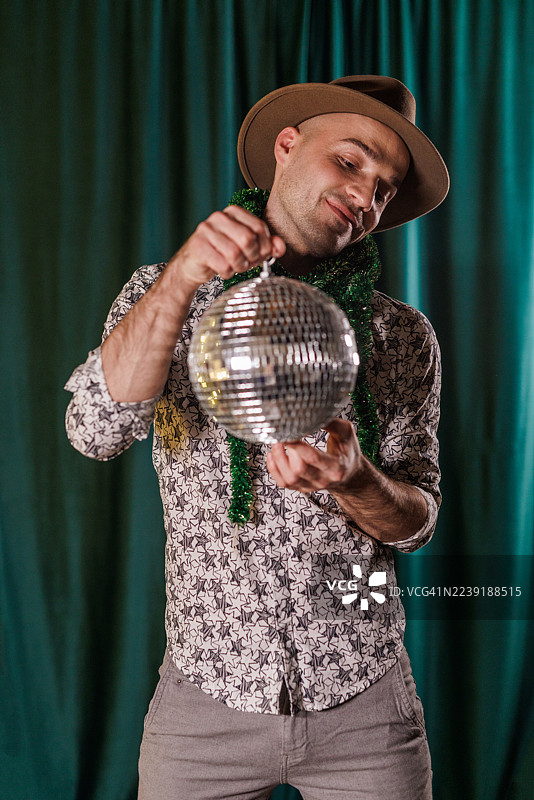 一个男人戴着帽子，挂着节日绿色的花环，和迪斯科球一起玩耍般地跳舞图片素材