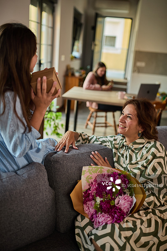 一位女士将鲜花赠予微笑的女儿，家人在舒适的家中放松图片素材