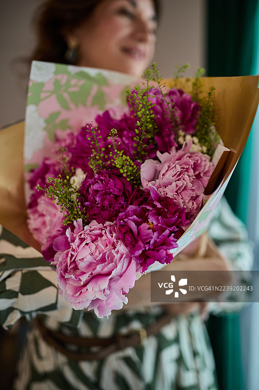 一位女士手持用装饰纸包装的鲜艳粉色牡丹花束，作为庆祝礼品。图片素材