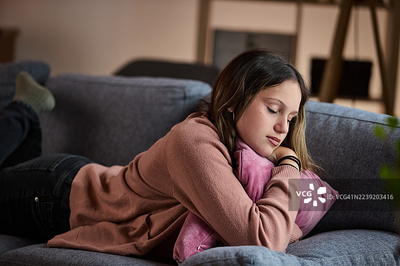 年轻女子在沙发上休息，抱着粉色枕头，享受宁静反思的舒适居家时光图片素材