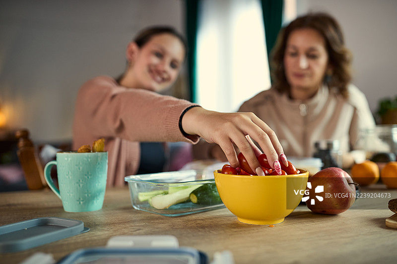 两位女性在温馨的厨房里，一边准备新鲜的番茄沙拉，一边分享着美好的时光。图片素材