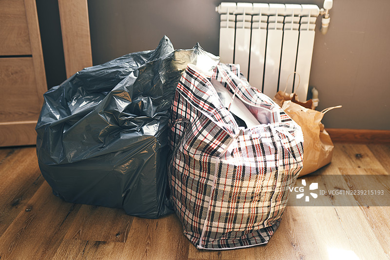 暖气片前、木地板旁堆放着家用杂物、垃圾袋和格子手提袋图片素材