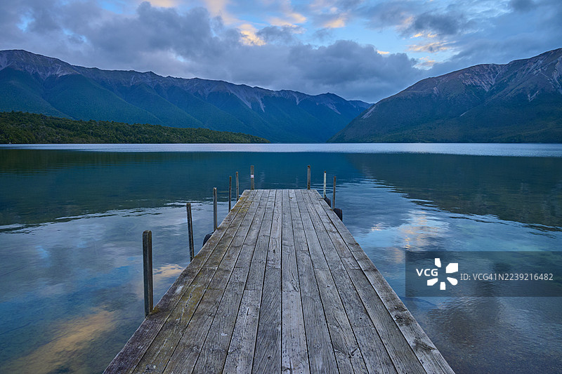 日出时分，木制人行桥伸入湖中，背景是群山，这是新西兰南岛塔斯曼地区圣阿尔诺罗托伊蒂湖的夏日风光，大洋洲。图片素材