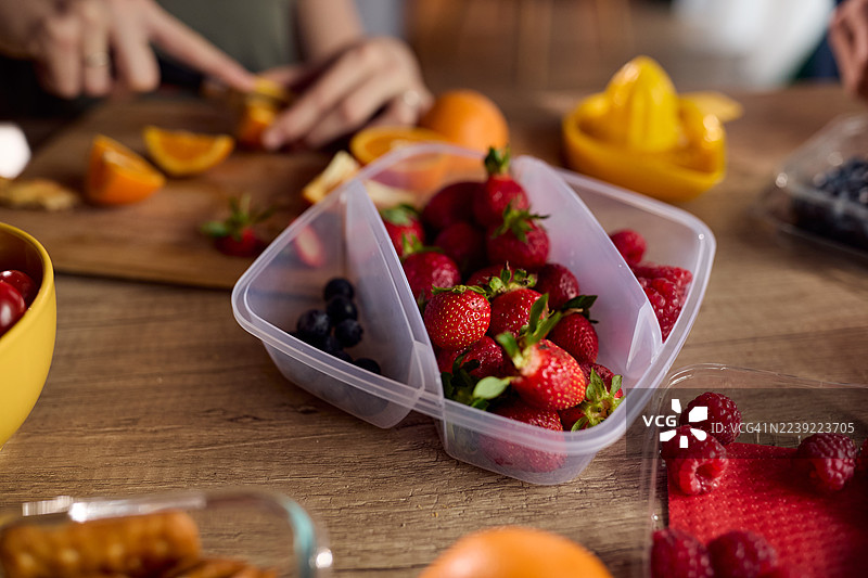 朋友们在木桌上随意准备水果，桌上有新鲜的浆果和柑橘图片素材