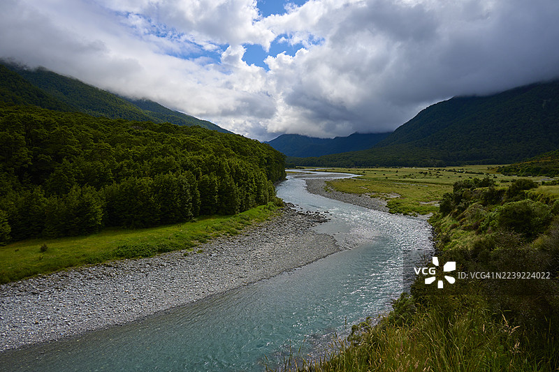 新西兰南岛哈斯特山口马卡罗拉河蓝池，河流穿过绿色的风景，远山葱郁，天空云彩密布，沿马卡罗拉路，哈斯特图片素材