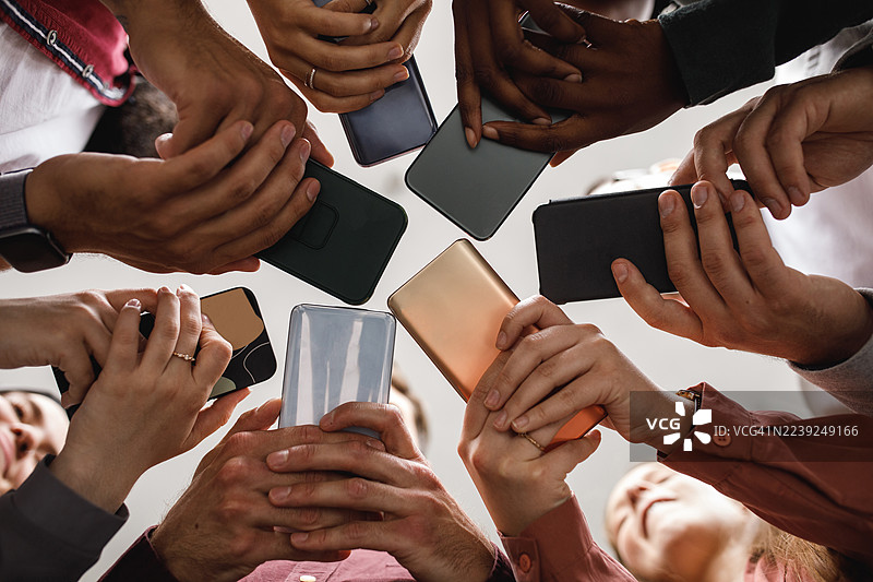一群来自不同背景的朋友和同事围成一圈，手持智能手机，共同协作。图片素材