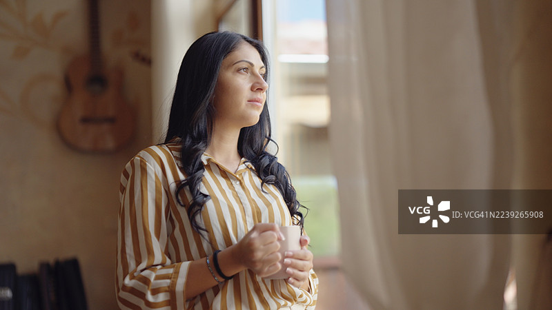 早晨咖啡。年轻女子在喝第一杯咖啡时望着大自然，陷入沉思。图片素材