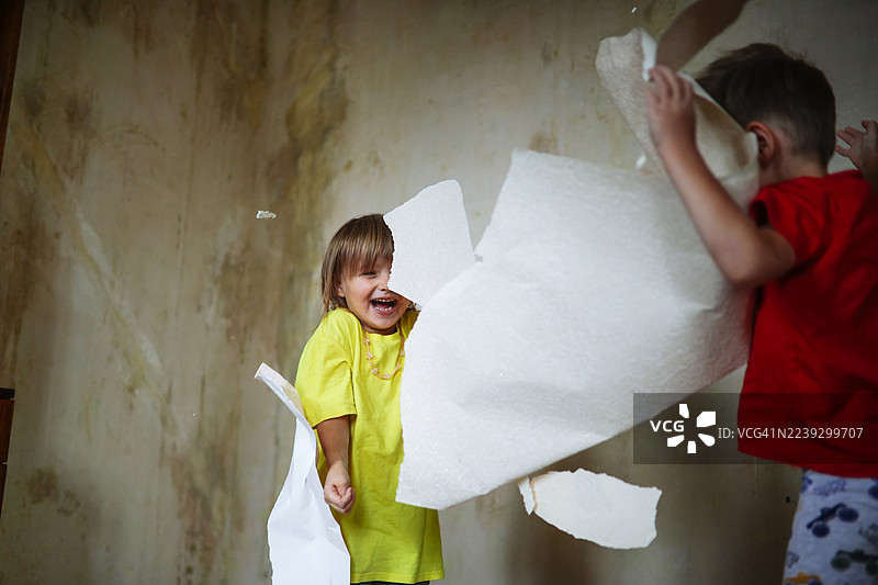 孩子们开心地撕掉旧墙纸并互相扔着玩。图片素材