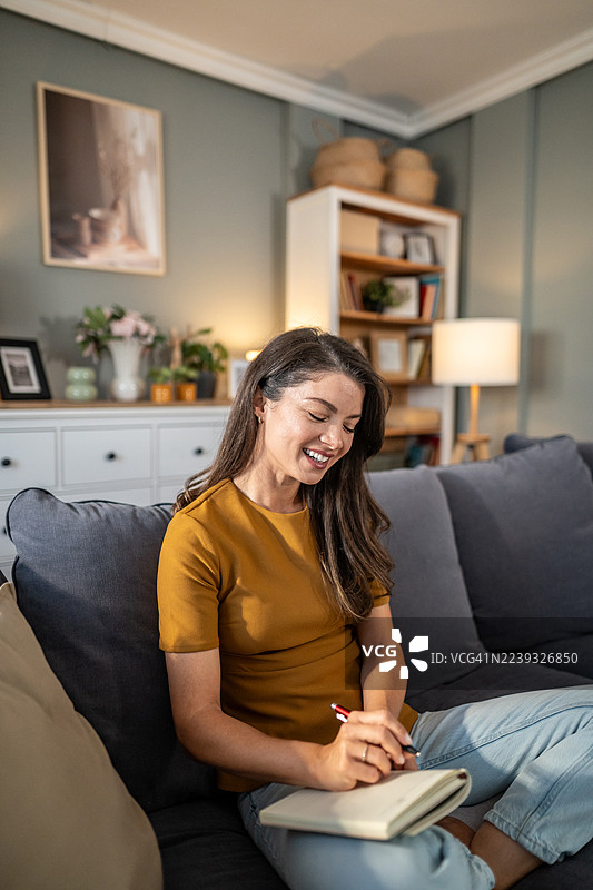 女人坐在沙发上，微笑着在日记本上写字图片素材