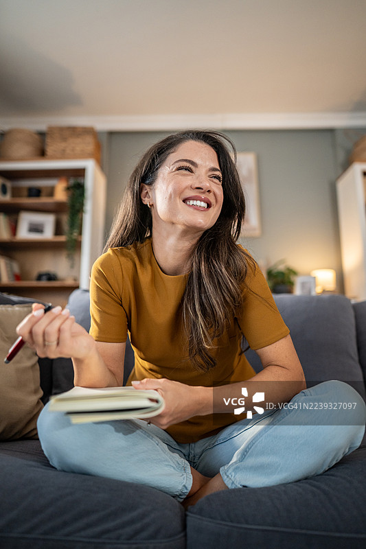 女人坐在沙发上，手里拿着笔和日记本，开心地笑着图片素材