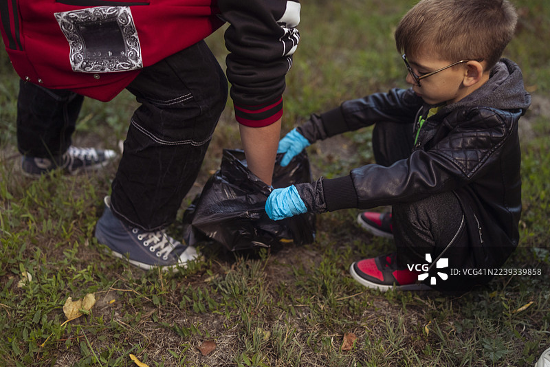年轻男孩在清理活动中，戴着手套在草地上收集垃圾图片素材
