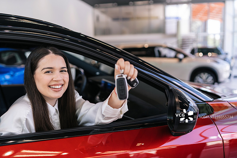 年轻女子在经销商处坐在新车里，微笑着，手里拿着车钥匙。图片素材