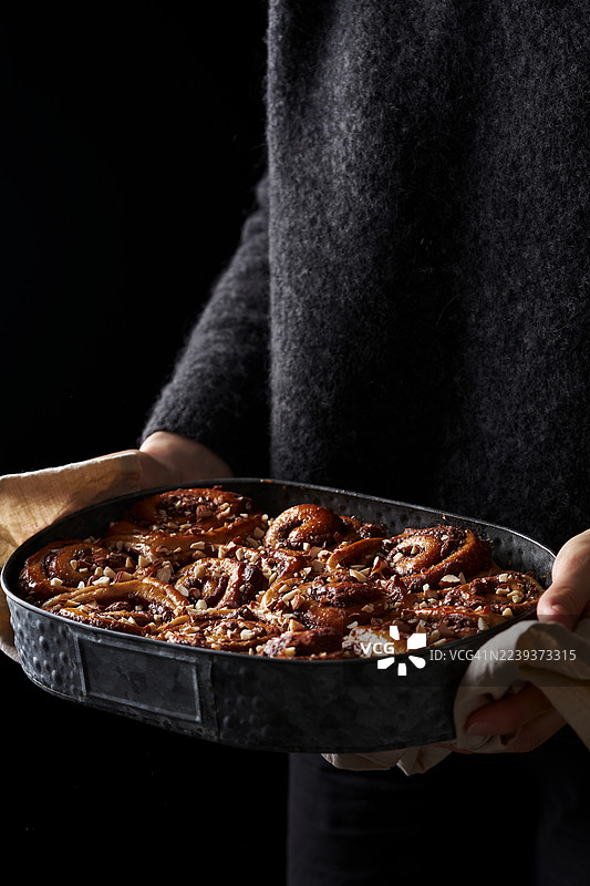 烤盘里放着刚出炉的肉桂卷，一个人正拿着图片素材