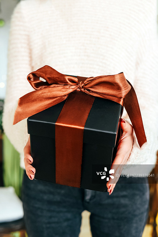 圣诞树背景下女性手中的礼物。惊喜。新年和圣诞节。礼物交换。图片素材