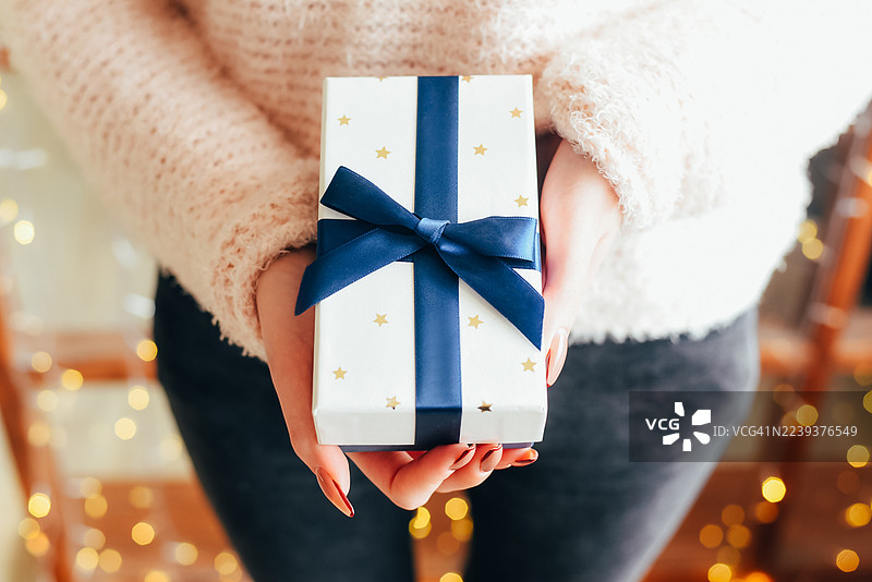 女人手中拿着礼物，背景是圣诞树。惊喜。新年和圣诞节。礼物交换。图片素材