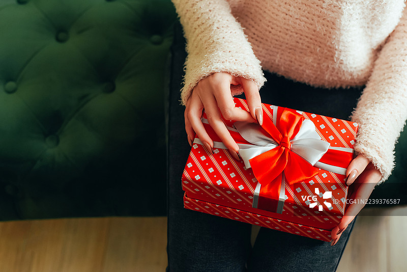 圣诞树背景下女性手中的礼物。惊喜。新年和圣诞节。礼物交换。图片素材