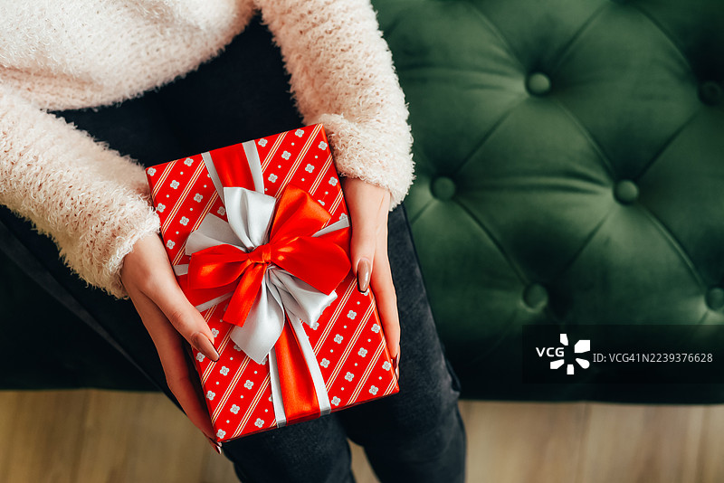 女人的手中拿着一份礼物，背景是圣诞树。惊喜。新年和圣诞节。礼物交换。图片素材