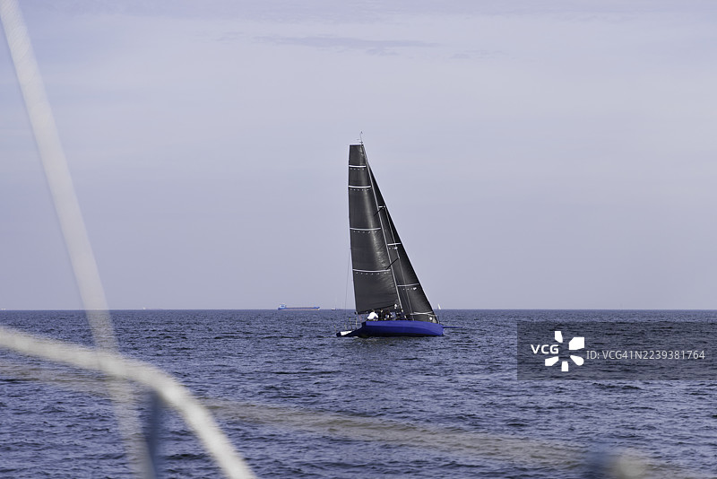 一艘帆船，黑帆蓝船体，在平静的海面上，天空晴朗图片素材