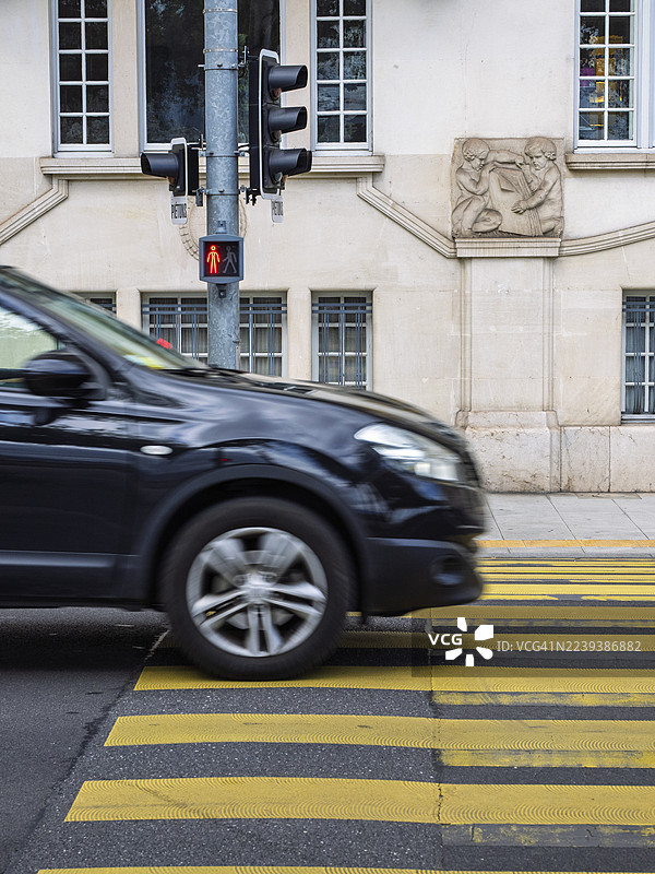 一辆行驶的汽车在城市中，红灯亮起时，正在通过人行横道。图片素材