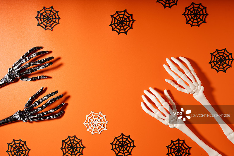 万圣节主题：橙色背景上的骷髅手和蜘蛛网图片素材