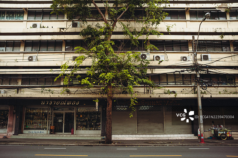 街边孤零零的树，旁边是关门的店铺和楼上的公寓图片素材