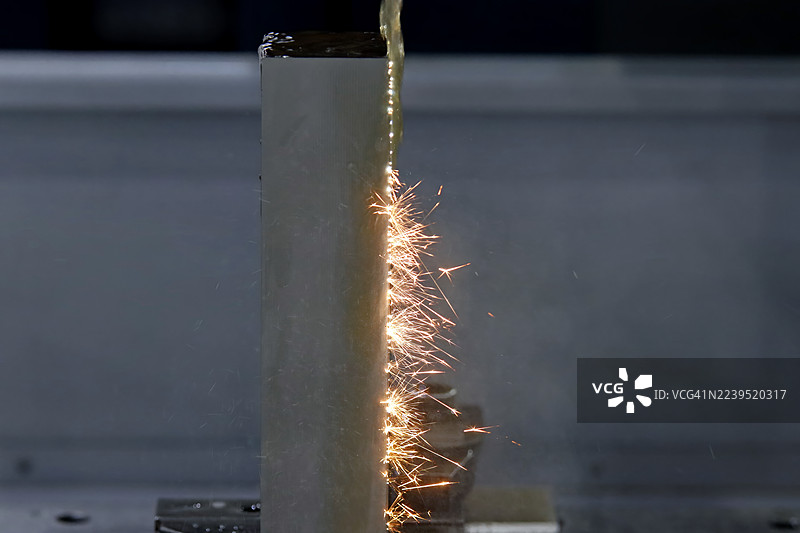 高精度电火花线切割。在加工高金属块过程中产生的强烈火花和喷射出的材料，展示了带有冷却液流动的先进金属加工技术。图片素材