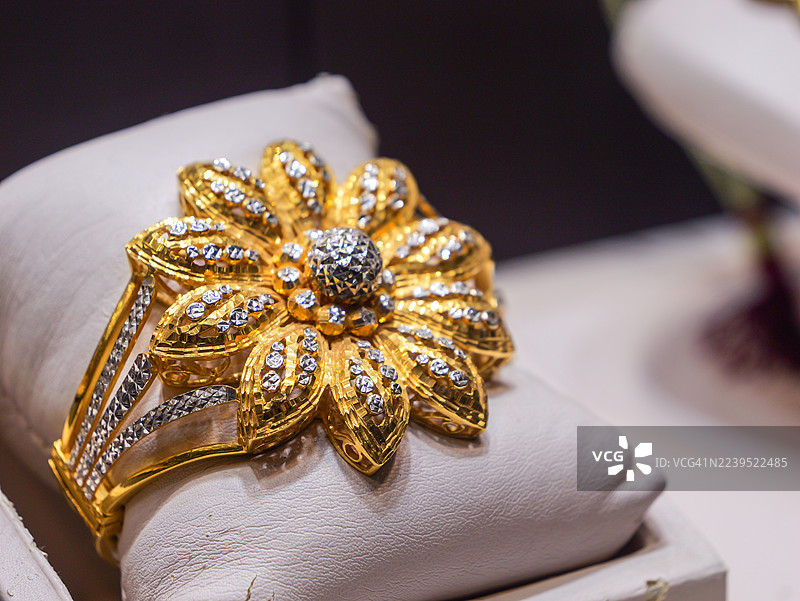 白色软垫上的金色花朵袖口手镯，镶嵌密镶钻石。图片素材