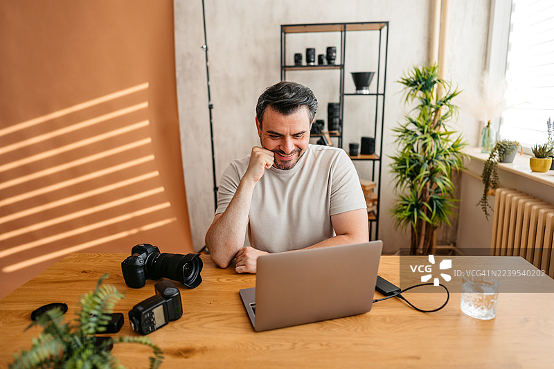 男摄影师在工作室使用笔记本电脑工作图片素材