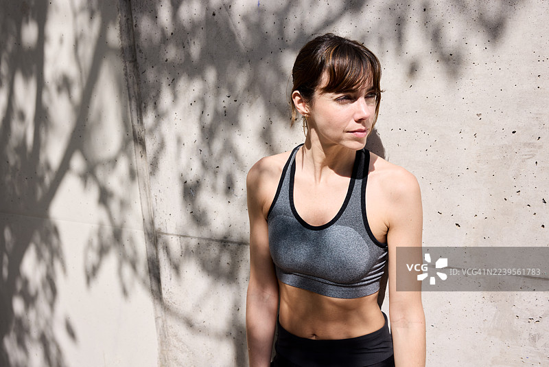 运动后，一位女士靠在水泥墙上休息。图片素材