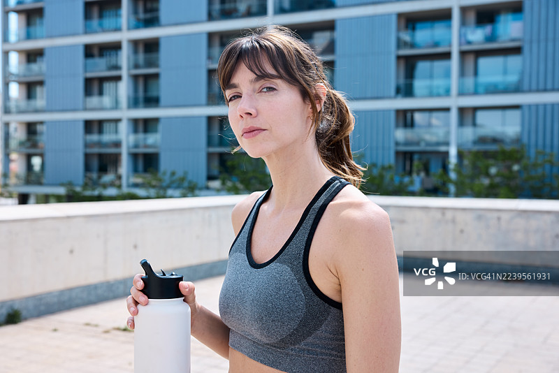一位注重环保的运动女性肖像，手持可重复使用的水瓶。图片素材