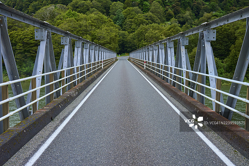 一条长长的钢桥穿过一片绿色的森林，位于新西兰南岛阿斯帕林山国家公园的哈斯特河畔的普莱森特弗拉特桥。图片素材