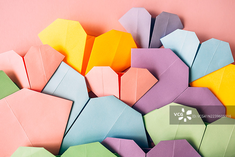 粉色背景上色彩缤纷的折纸心形。非常适合用于爱情、情人节、手工制作、创意、关系和浪漫装饰等主题。图片素材