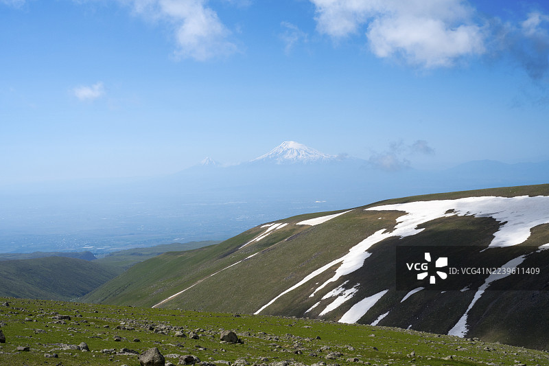 远方雪原和多云天空下的绿色山地景观，远眺土耳其的亚拉腊山、阿拉加兹山（阿拉加茨山，阿拉加茨，阿拉格亚兹），一座海拔4090米的高山，位于阿拉加佐特省、希拉克省，亚美尼亚。图片素材