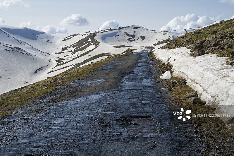 一条孤寂、坑洼的道路穿过崎岖的雪山地带，天空布满乌云，通往阿拉加茨山，阿拉加茨，阿拉加茨，阿拉吉亚兹，休眠的层状火山，海拔4090米，阿拉加措特恩省，希拉克省，亚美尼亚图片素材
