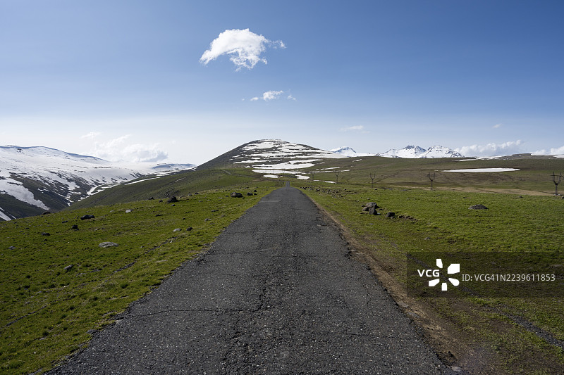 一条道路穿过广阔的绿色风景，有雪地，天空晴朗，通往阿拉加茨山，阿拉加茨，阿拉加茨，阿拉吉亚兹，死火山锥，4090米，阿拉加措特恩省，希拉克省，亚美尼亚图片素材