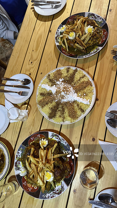 分享的摩洛哥菜肴盛宴，鸡肉塔吉锅饰以薯条和鸡蛋，甜味塞法梅德福纳撒上糖粉和肉桂，准备好享用节日大餐图片素材