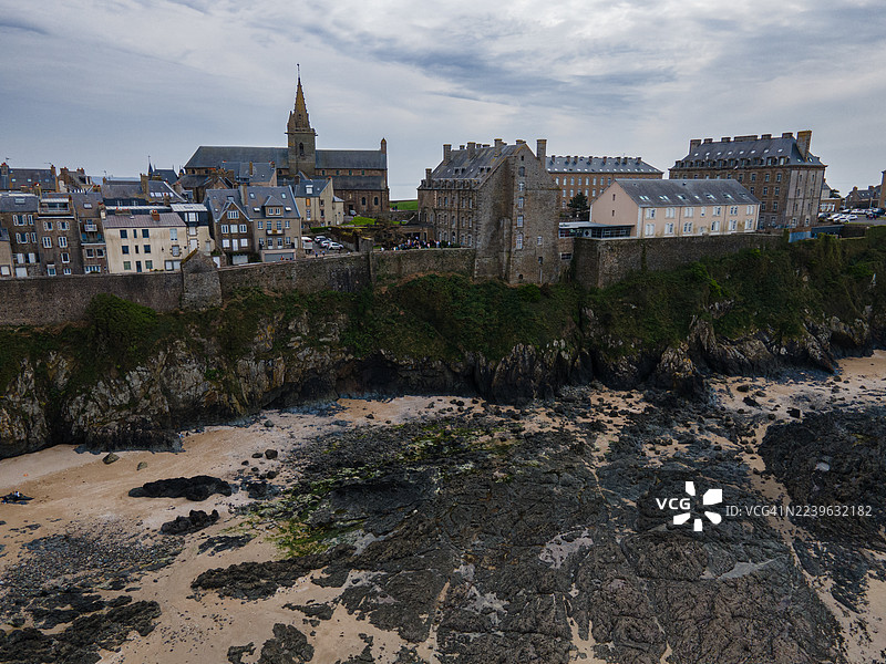 布列塔尼地区迪南古城的鸟瞰图，法国，古建筑和教堂尖塔俯瞰着多云天空下的岩石海岸和海滩。图片素材
