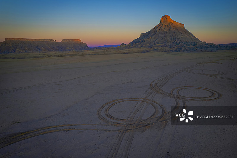 日落时分戏剧性的沙漠景观，前景有轮胎痕迹，背景是雄伟的岩层和充满活力的天空，美国，美国，韦恩县图片素材