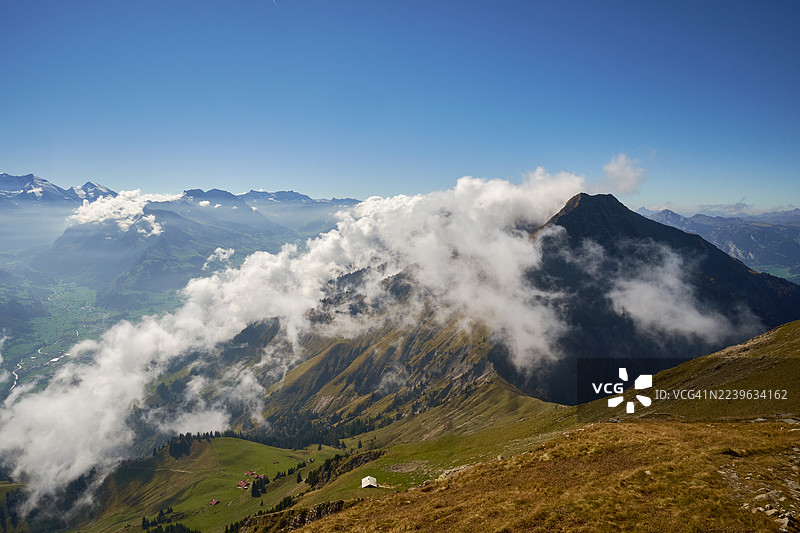 瑞士，维米，在晴朗的蓝天下，雄伟的雪山被云雾笼罩，俯瞰着郁郁葱葱的绿色山谷。图片素材
