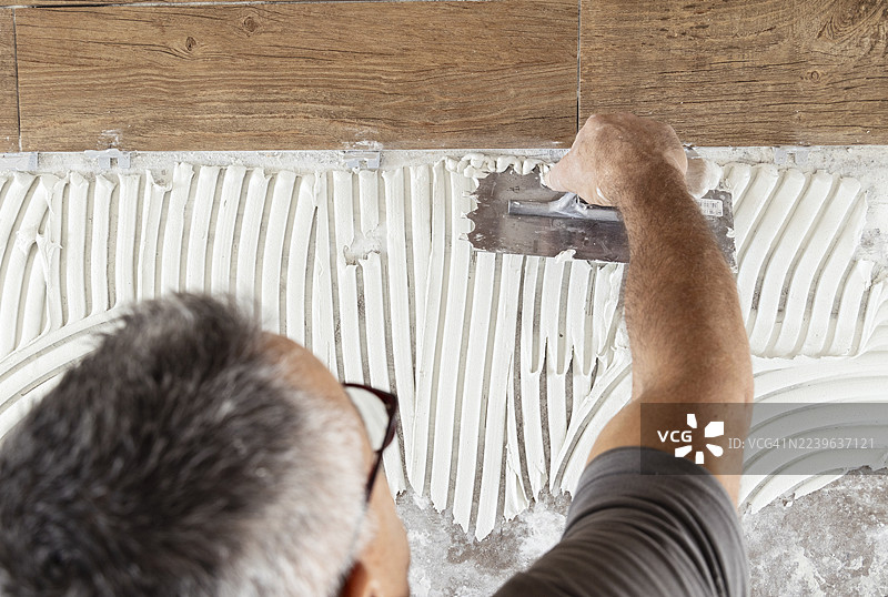 特写：男子正在墙上涂抹粘合剂，准备铺设瓷砖图片素材