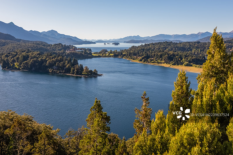 阿根廷巴里洛切，全景视图，宁静的湖泊，四周环绕着郁郁葱葱的绿色森林和雄伟的山脉，在晴朗的蓝天下，唤起宁静和自然之美的感觉，阿根廷，巴里洛切图片素材