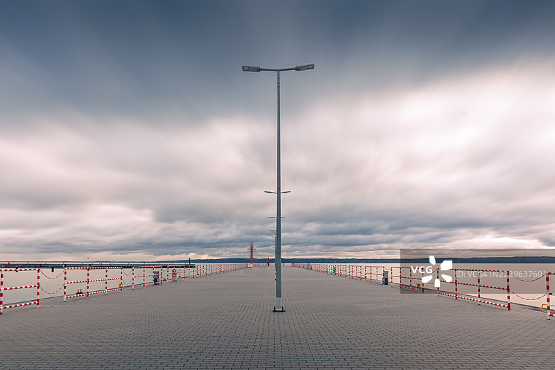 波兰克里尼察莫尔斯卡，平静湖面上延伸的长码头，远处有灯塔，天空布满戏剧性的云彩。图片素材