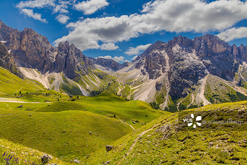 郁郁葱葱的山谷，坐落于雄伟的山脉之间，头顶是蓝天白云，意大利，瓦尔加尔代纳的塞尔瓦，尼维斯之路图片素材
