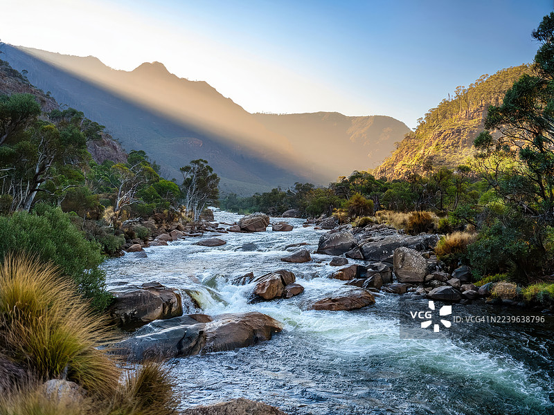 阳光洒在湍急的山间河流上，两岸绿意盎然，河岸布满岩石，天空晴朗，澳大利亚，东吉普斯兰，雪河国家公园图片素材