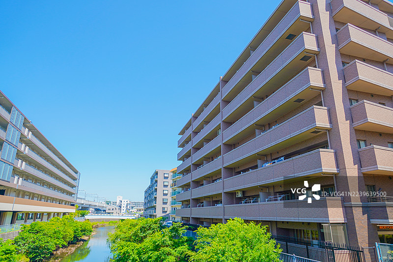 现代公寓楼，宁静的河流旁绿树成荫，天空湛蓝，展示了都市生活与自然和谐共存的景象，日本，保土谷，星川图片素材