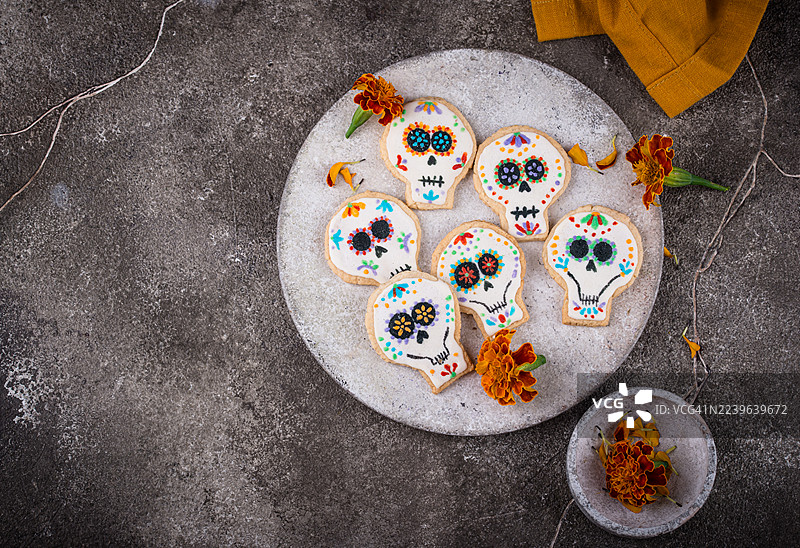 从高处俯视，灰色的水泥桌上摆放着色彩缤纷的糖骷髅饼干和万寿菊，以此庆祝亡灵节。图片素材