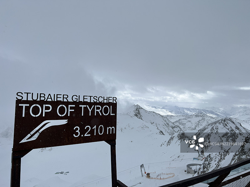 3210米高的斯图拜冰川和蒂罗尔之巅指示牌，背景为白雪皑皑的山脉和多云的天空图片素材