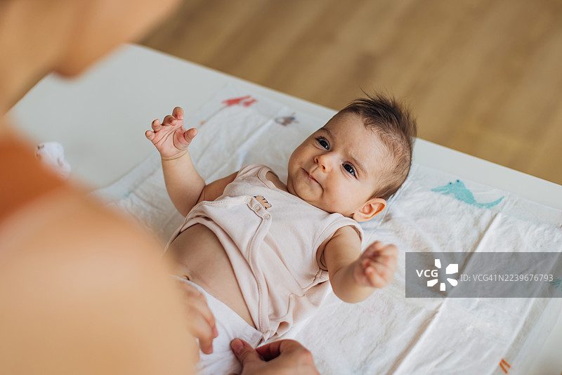 宝宝在家与妈妈亲密互动，妈妈正在为她换尿布和衣服。图片素材