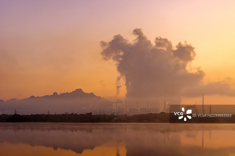 泰国兰邦府，Mae Mo发电厂的黄昏景象。煤电站的蒸汽烟雾与薄雾倒映在湖水中，彰显了泰国北部工业、能源和环境的影响。图片素材