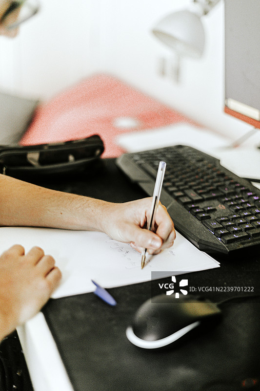 近距离拍摄一名左撇子青少年在电脑前做数学练习的手部特写图片素材